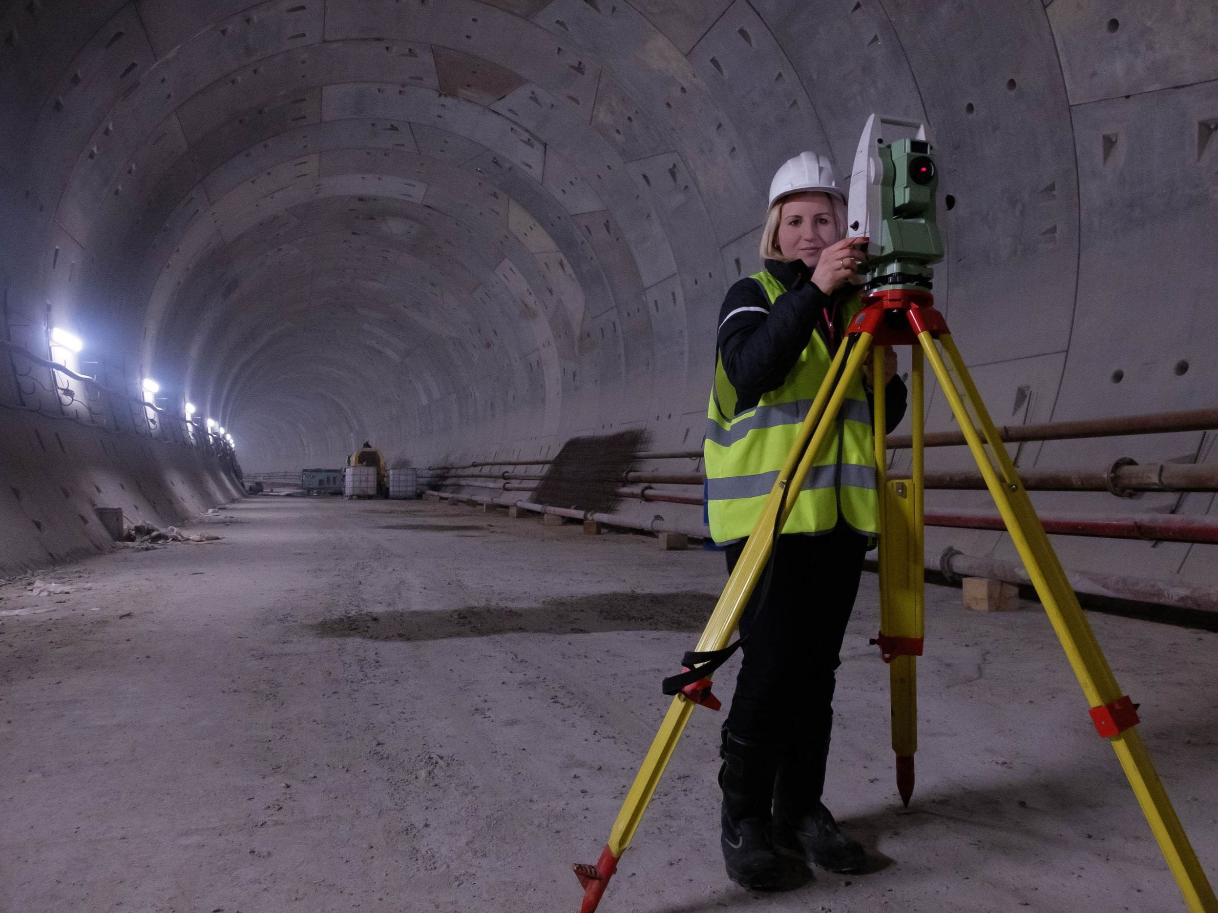 woman works on the geodetic total station in the tunnell of metro under construction