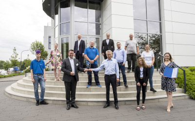 Managing Director Eugen Dumitrescu receives the glass trophy in front of the TRIOPTICS GmbH company building in Wedel from IHK Vice President Jan-Henrik Fock (third from left) as an award for TOP training company. Employees and trainees of the company were also present at the ceremony. (Picture: IHK/Peter Lühr)